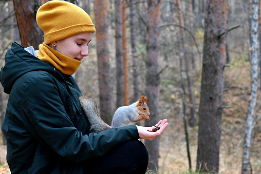 A young teenage girl feeds a squirrel with her hand in the forest.