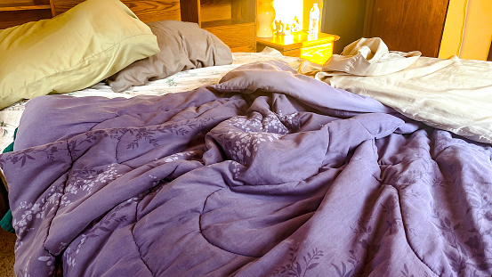 The guests have departed and the unmade bed is left behind.  The early morning sunshine illuminates the messy room.