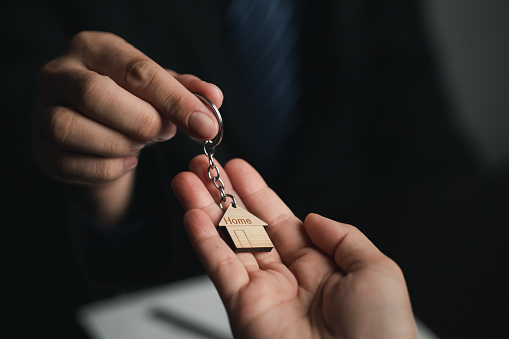 A home rental company employee is handing the house keys to a customer who has agreed to sign a rental contract, explaining the details and terms of the rental. Home and real estate rental ideas.