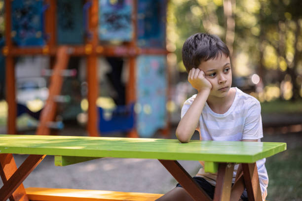 Sad boy holding his head while sitting on table in the park