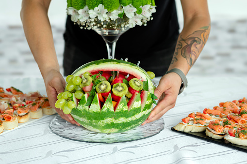 Close-up of man serving beautifully decorated watermelon with fruits at banquet