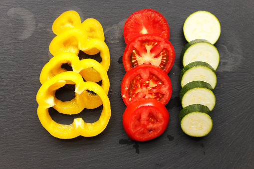 Sliced vegetable: pepper, tomato and zucchini on a stone plate.