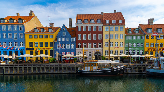 Colorful old houses at Nyhavn in Copenhagen, the canal and a ship in front of it, partly cloudy blue sky, horizontal,