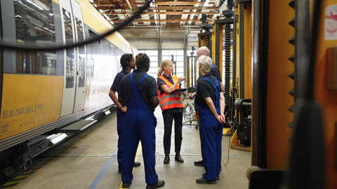 Railway workshop manager discussing work with team of mechanics