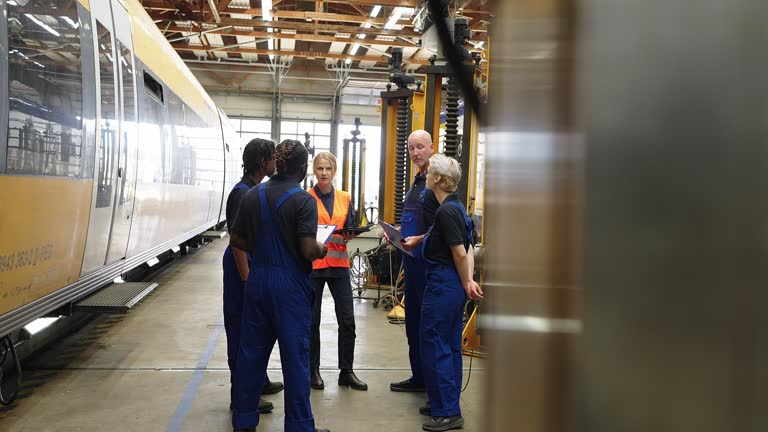 Senior manager discussing maintenance of public transport trains with team of mechanics in workshop