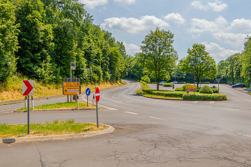 Empty country road with various traffic signs: no entry, caution, driving direction and direction to towns, public parking lot and leafy trees in the background, sunny spring day in Bitburg, Germany