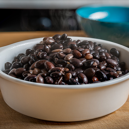 Cooked black beans in a white bowl on a wooden table being mixed