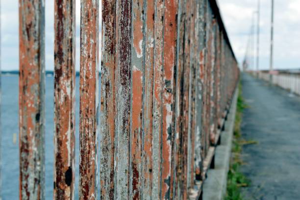 An aged, rusted wall situated next to a body of water, with a concrete pathway running between them
