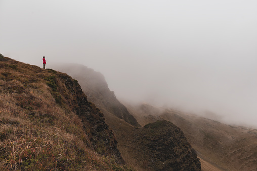 Lonely woman standing on the edge. Woman on the mountain looks down on the foggy valle