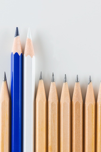 One blue and one white pencil are being out of line of pencils on white background.