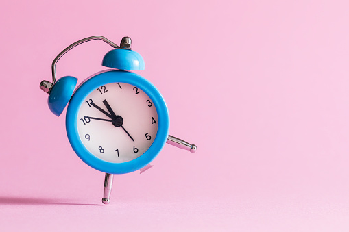 Blue alarm clock  in front of pink  wall. The clocks time is showing 5 to 12.