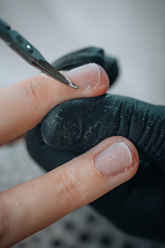 Close-up of manicurist hands with manicure scissors removing cuticles on woman's nails in beauty salon