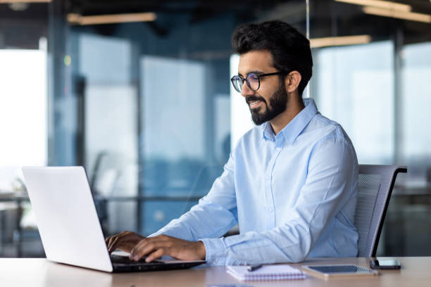 istock Young Indian male student, freelancer learning remotely online using laptop in office sitting at desk 1595930833