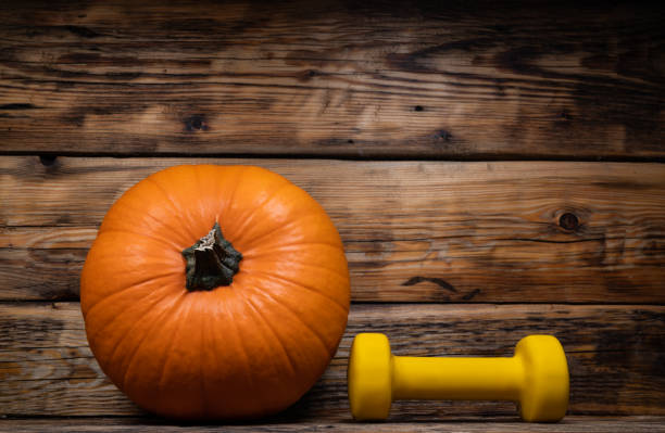 istock Gym dumbbell and autumn pumpkin. Fall composition with copy space on wooden background. 1595940582