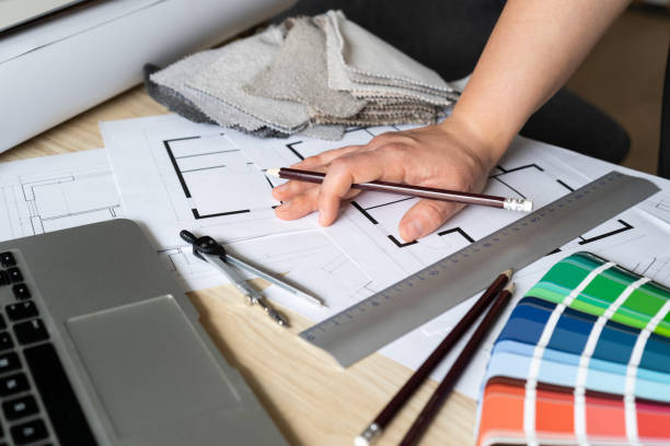 istock Female architect or interior designer working on home floor plans at her studio desk with blueprints, color scheme palette, laptop, and fabric samples. 1595956639