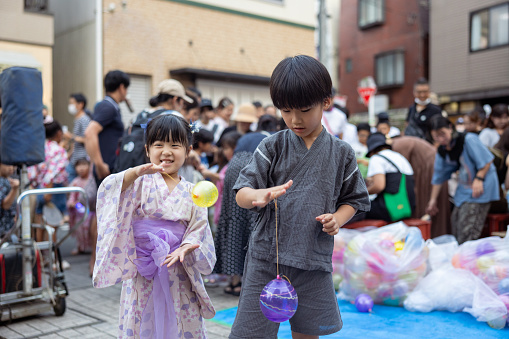 Boy and his little sister in Jinbei / Yukata playing yo-yo water balloon in summer festival