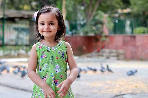 Cute smiling baby girl standing outdoors in the public park during day time.