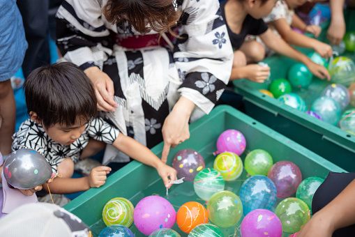 Mother and her little son in Yukata / Jinbei playing Yo-yo fishing at summer festival