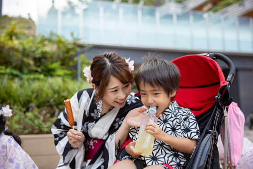 Mother and her little son in Yukata eating/drinking in summer festival