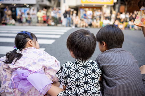 Rear view of three kids waiting for street performance at summer festival