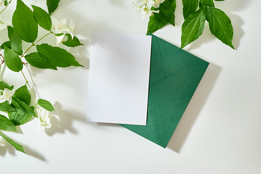 Flat lay blank white greeting card and envelope on a white background with sunlight and shadows of jasmine leaf flowers