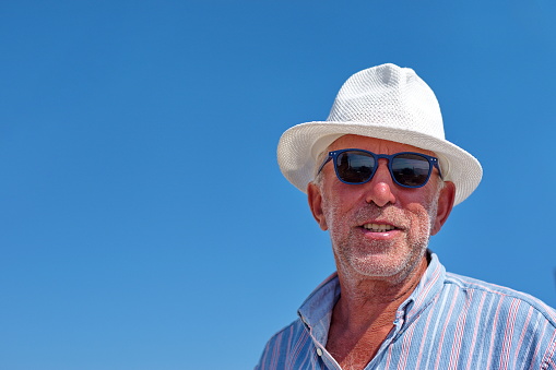 Waist up portrait of a senior man with a hat against the blue sky