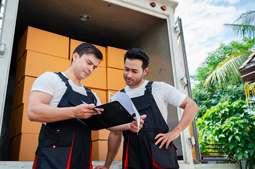 Unloading boxes and furniture from a pickup truck to a new house with service cargo two men movers worker in uniform lifting boxes. concept of Home moving and delivery.