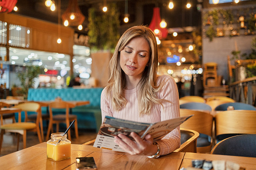 Cute Pretty Brunette Young Woman in Casual Outfit Chilling at Cozy Coffee Shop, Sitting Alone at Table, Drinking Coffee, Reading Menu, Businesswoman Having Lunch Break at Cafe, Copy Space
