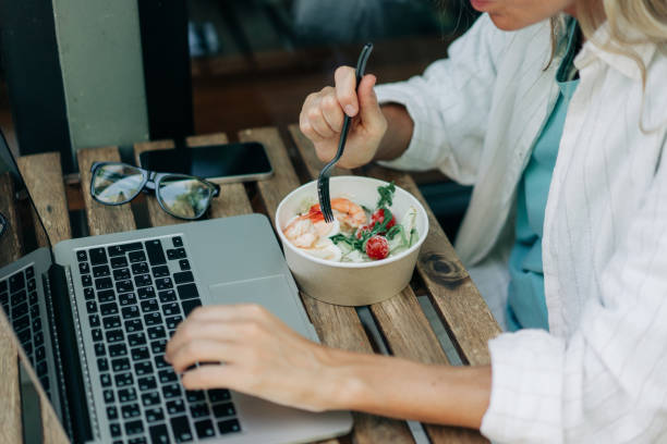 istock Unrecognizable woman eats salad and works on a laptop in a cafe. 1596141972
