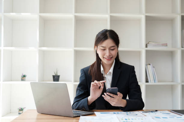 istock Young beautiful Asian businesswoman working with laptop computer while using smartphone in her office room. 1596148799