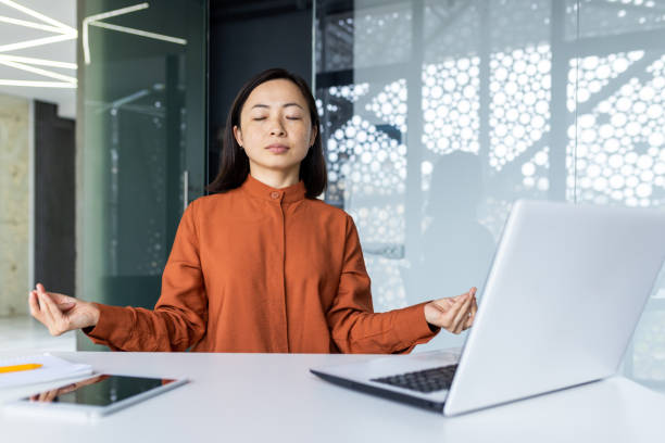 istock Young beautiful Asian web developer working inside office building, woman resting meditating at workplace with eyes closed, female worker using laptop to write code. 1596158583