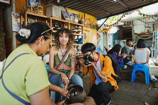 Asian man and his girlfriend looking at a monk bowl made by a local craftsperson while traveling in the community.