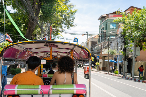 Happy Asian couple travel by Tuk Tuk to admire Thai culture around Bangkok.