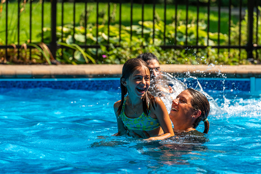 A couple with their two daughters having fun and swimming in their back yard pool during a sunny day of summer.