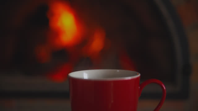 DS A cup of coffee with a background of a fireplace with flames of fire