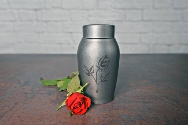 istock Funeral urn beside a red rose. Horizontal image with selective focus. 1596186695