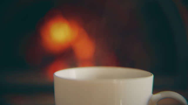 CU Steam rises from a cup of hot coffee with a background of a fireplace