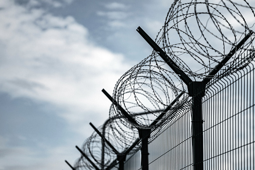 Barbed Wire Fence. Jail or border fence with razor wire against dark sky. Security concept
