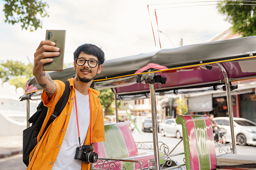 Young Asian man traveler in Bangkok downtown district, holding a mobile phone