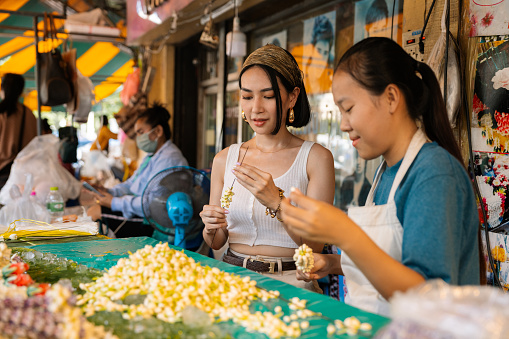 Asian tourist discovers Thai culture by learning floral garland making in Bangkok.