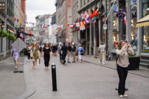 Defocused shot of people walking the streets of Old Montreal with woman stopping to take a picture. Shot in the morning in early summer.