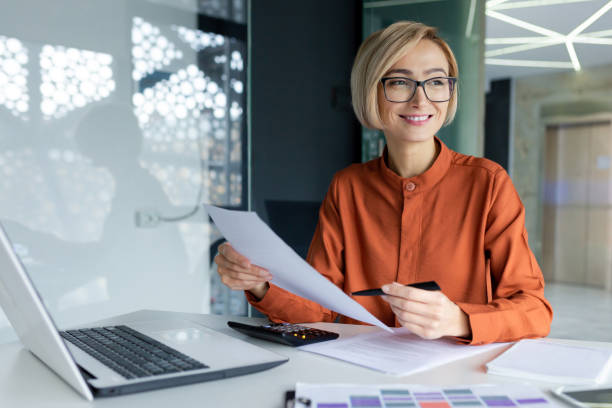 istock Young successful business woman working inside office with documents, woman satisfied with achievement results reviewing contract, bills and documents, financier in glasses smiling 1596264140