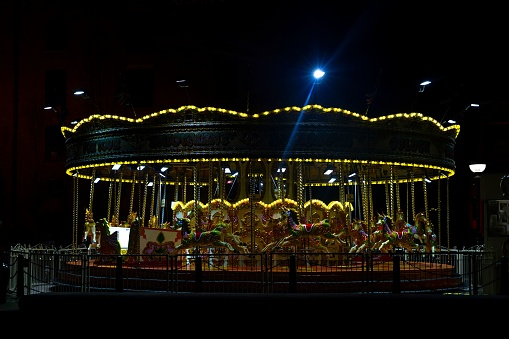 The bright lights of a fast moving fairground merry-go-round blur against a dark night sky. The motion blurred yellow lights are spinning underneath the rides carousel.