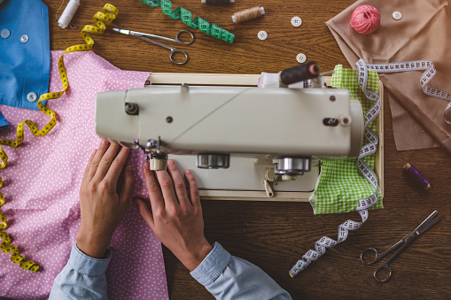 Seamstress using a sewing machine and various sewing accessories for clothes production during sewing process. Top view