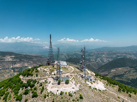 Aerial view of telecommunication antennas in Albania. Television, radio and communications antenna with numerous transmitters, Technology. Drone view of group of telecommunications towers surrounded by green forest trees, 5G antennas.