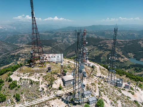 Aerial view of telecommunication antennas in Albania. Television, radio and communications antenna with numerous transmitters, Technology. Drone view of group of telecommunications towers surrounded by green forest trees, 5G antennas.
