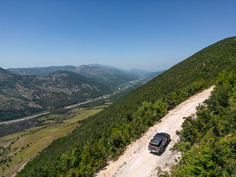 Aerial view of an off-road pick-up truck driving in the mountains. Gravel road through the forest line.