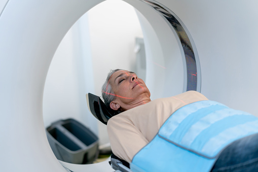 Mature woman lying down on a CAT scan machine with eyes closed at the hospital - Healthcare and lifestyles concepts
