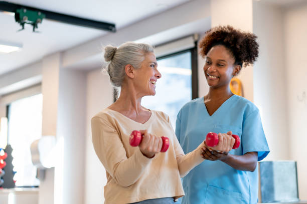 istock Black physical therapist correcting the posture of her patient while she is working out with dumbbells during physical therapy 1596311875