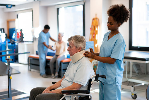African-American physical therapist adjusting a neck brace on a senior patient on a wheel chair after finishing therapy - healthcare concepts - Incidental patient and therapist at background